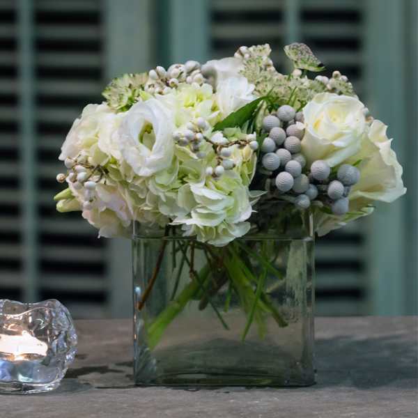 White floral arrangement in a square glass vase beside a candle holder