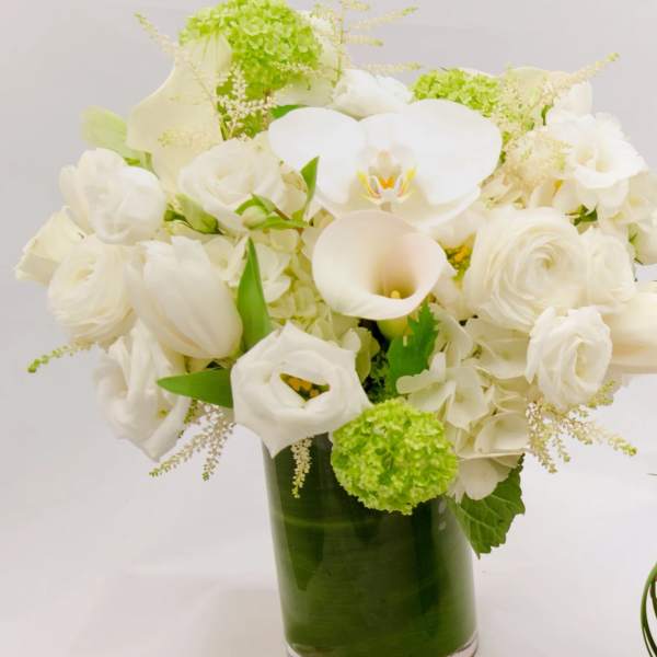 White floral arrangement in a glass vase with green accents