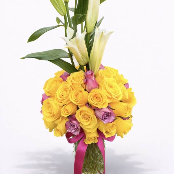 Yellow and pink roses with white lilies in a clear vase