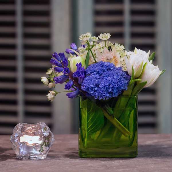Blue and white flowers in a green glass vase beside a small candle holder