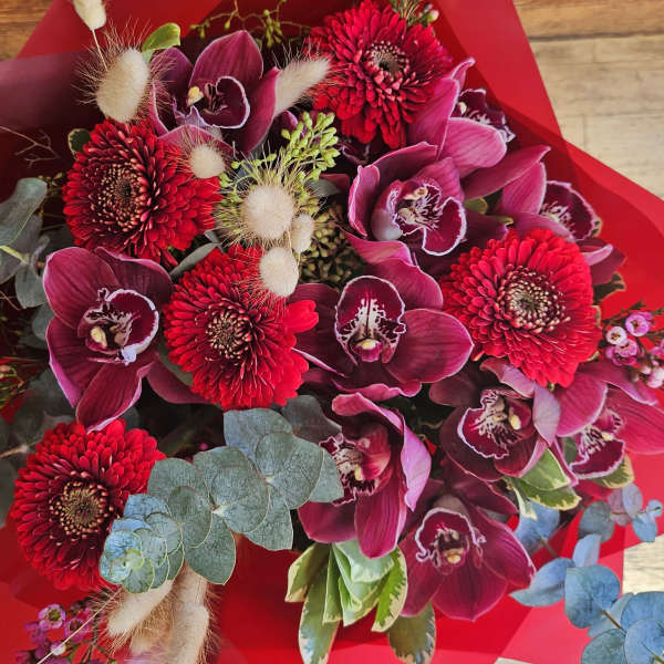Bouquet of red gerbera daisies and magenta orchids wrapped in red paper