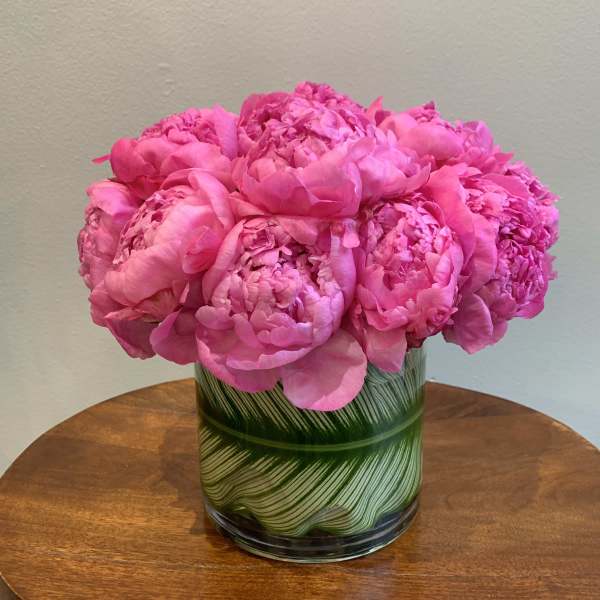 Pink peonies arranged in a glass vase with green leaf pattern
