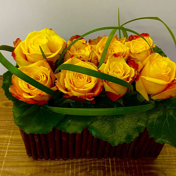 Yellow roses in a red basket with green decorative loops