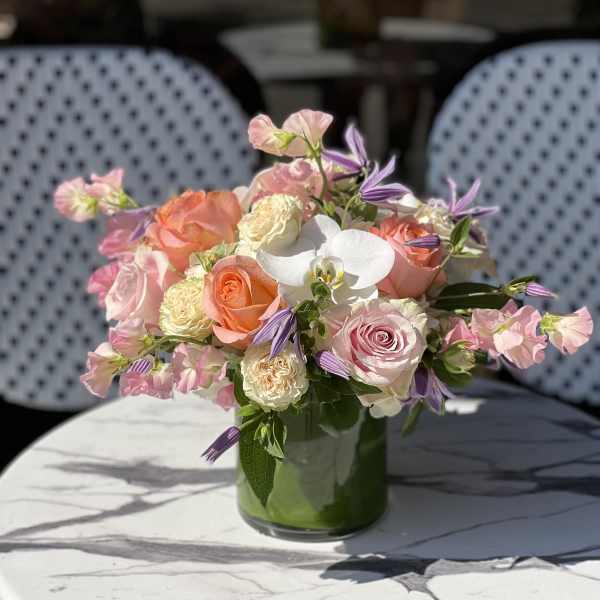 Pink and peach roses with white orchids in a glass vase