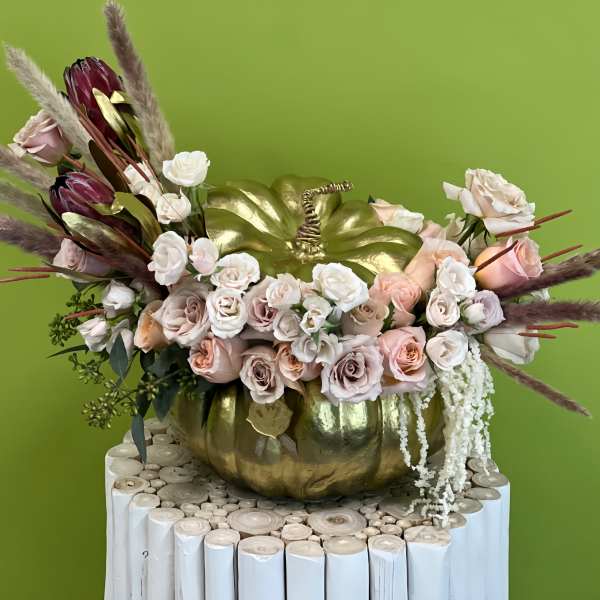 Floral arrangement in a gold pumpkin container with pale roses and burgundy blooms