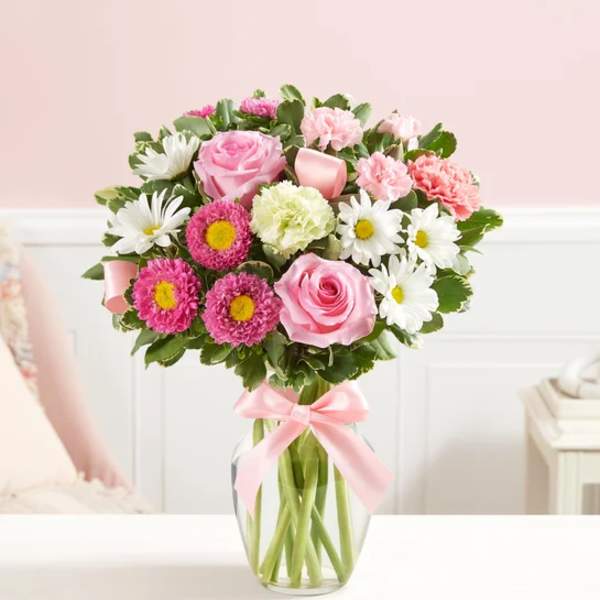 Pink and white mixed bouquet in a clear glass vase with a pink ribbon