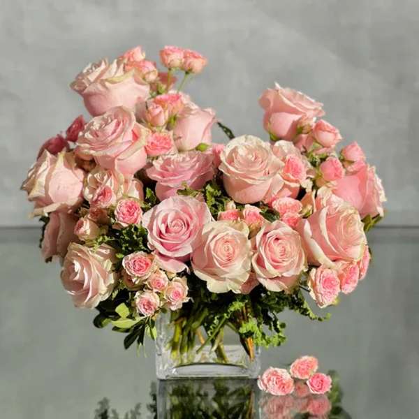 Bouquet of pale pink roses and spray roses in a clear glass vase