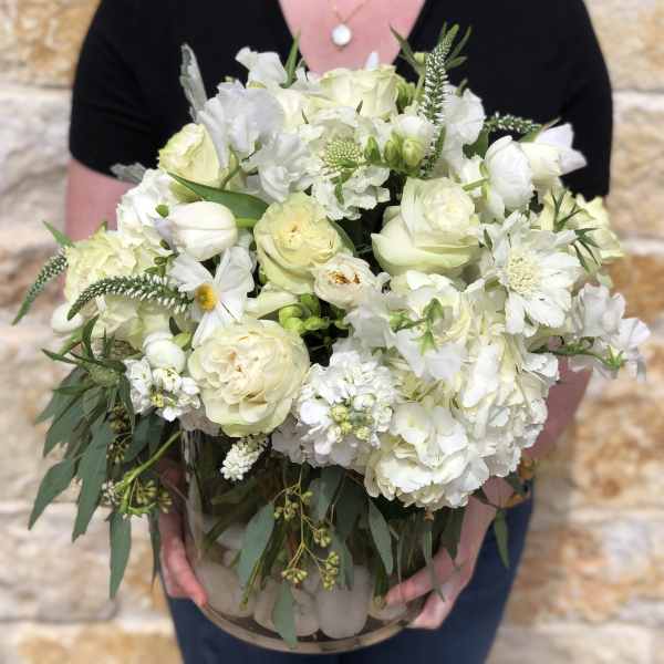White floral bouquet in a clear glass vase held by a person