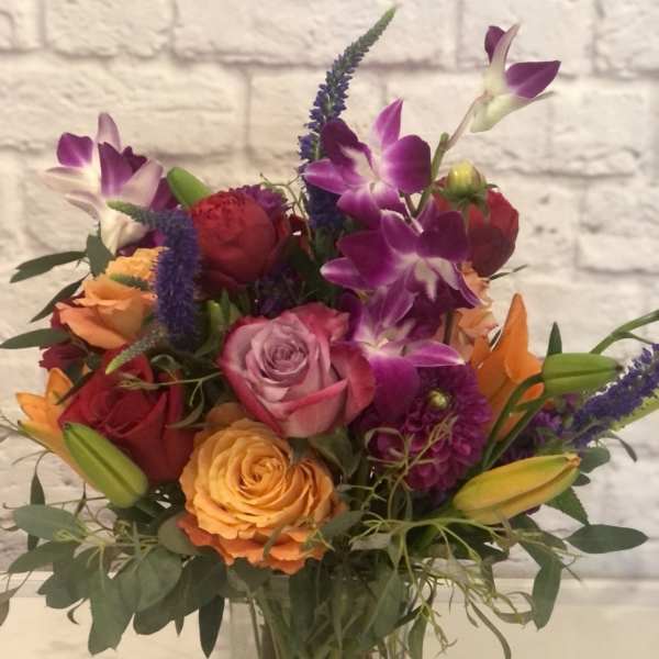 Mixed bouquet of roses, orchids, and lilies in a clear glass vase
