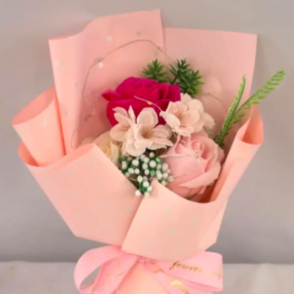 Small bouquet of pink and white roses and blossoms wrapped in pale pink paper with a bow