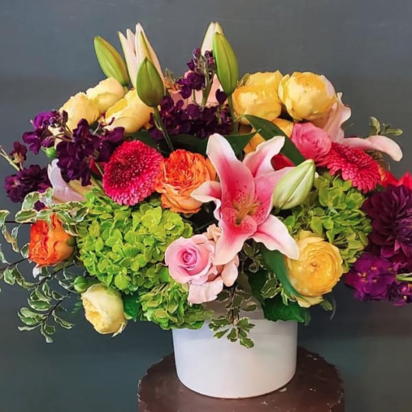 Colorful arrangement of lilies, roses, hydrangeas, and other blooms in a white ceramic vase