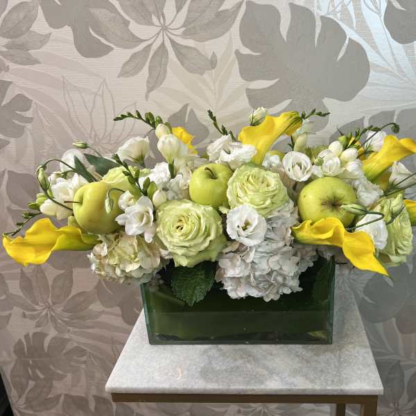 Yellow calla lilies and white flowers arranged in a green rectangular vase