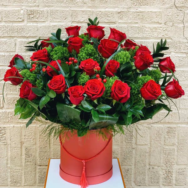 Red roses arranged in a round box with green filler and foliage