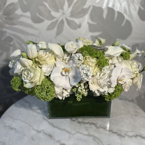 White roses, orchids, and calla lilies in a green rectangular vase