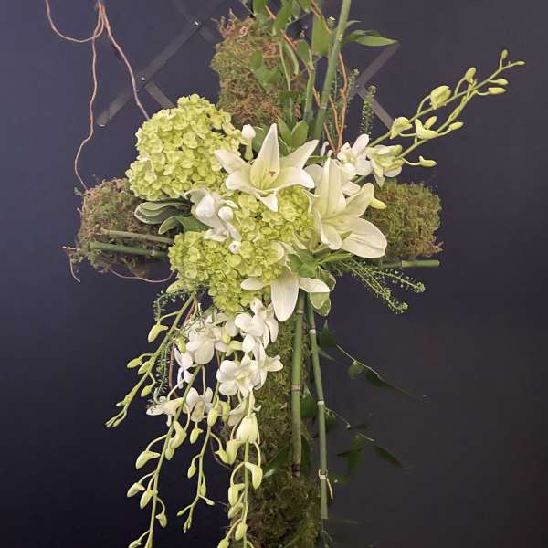 Cross-shaped floral arrangement with white lilies, green hydrangeas, and orchids