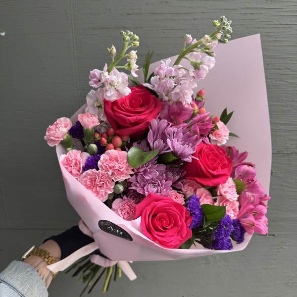 Pink bouquet with roses, carnations, and purple flowers in pastel wrap