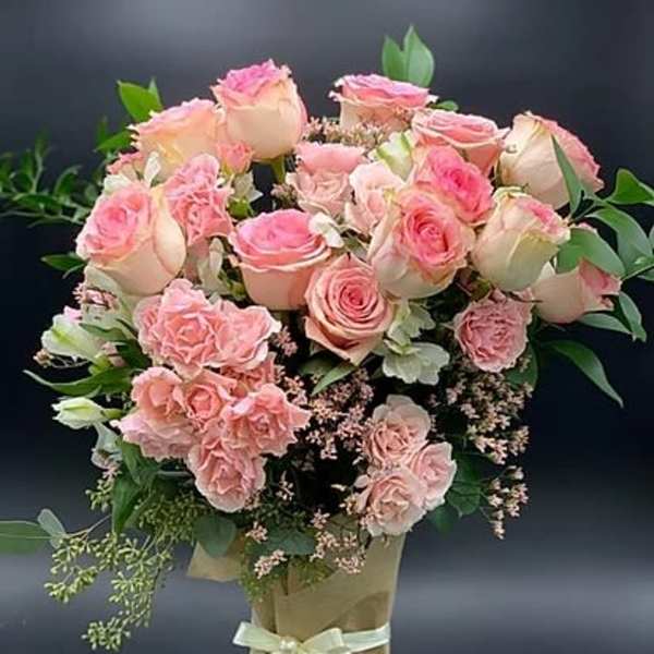 Pink roses and carnations arranged in a wrapped bouquet with a ribbon