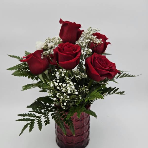 Red roses arranged in a purple glass vase with white filler flowers