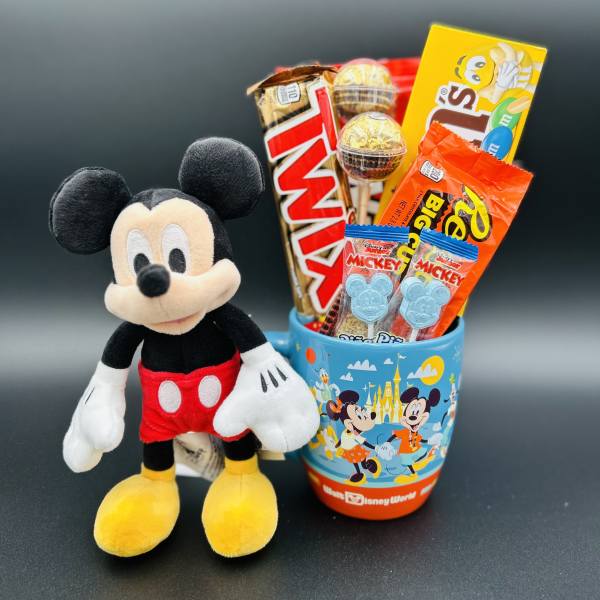 Mickey Mouse plush beside a Disney-themed cup filled with candy bars and lollipops