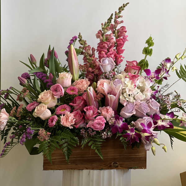Large mixed bouquet with pink roses, lilies, orchids, and snapdragons in a wooden container