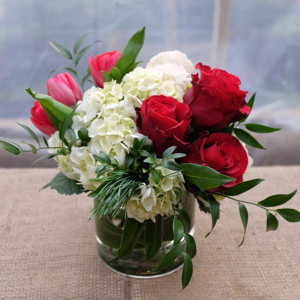 Red roses and pink tulips arranged with white hydrangeas in a glass vase.