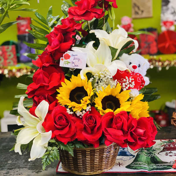 Basket arrangement with red roses, white lilies, yellow sunflowers and a white teddy bear.