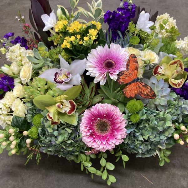 Mixed floral arrangement with pink gerberas, orchids, and a butterfly accent