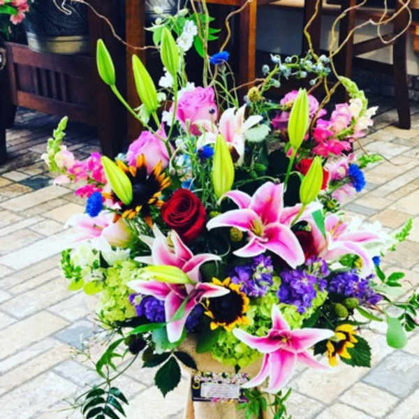Large bouquet of pink lilies, roses, and sunflowers in a wrapped container