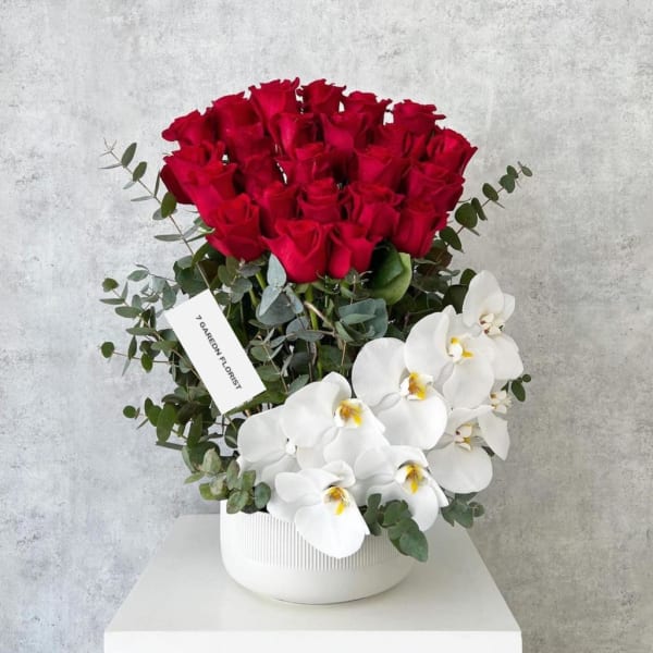 Red roses and white orchids arranged in a white vase