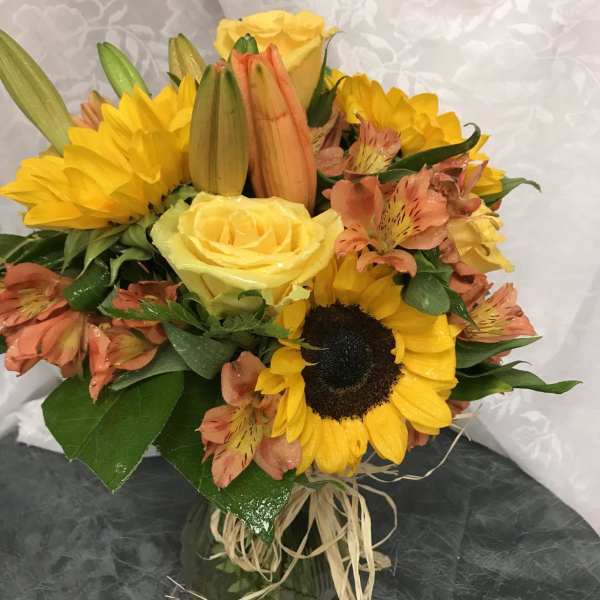 Bouquet of yellow roses, sunflowers, and peach alstroemeria in a glass vase