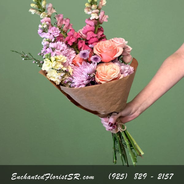 Handheld bouquet of pink, peach, and lavender flowers wrapped in brown paper