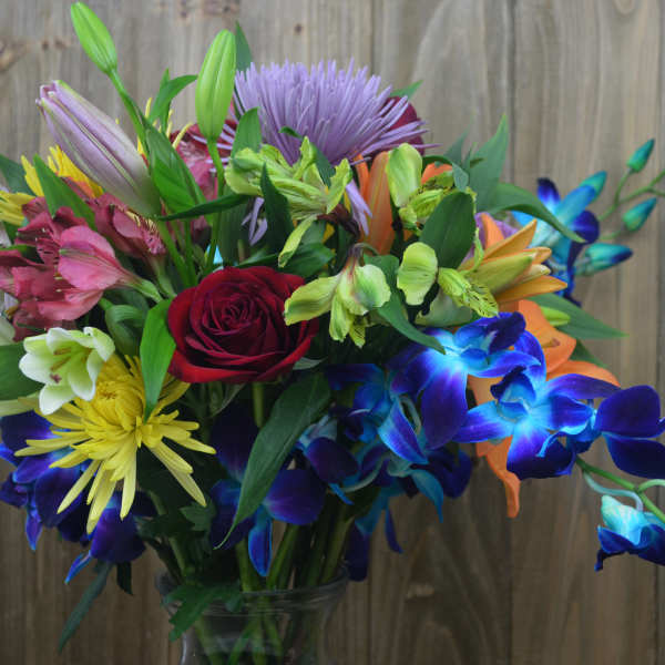 Colorful mixed bouquet with roses, lilies, and orchids in a glass vase