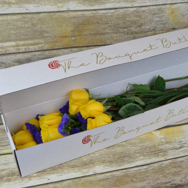 Yellow roses with purple filler in a white bouquet box