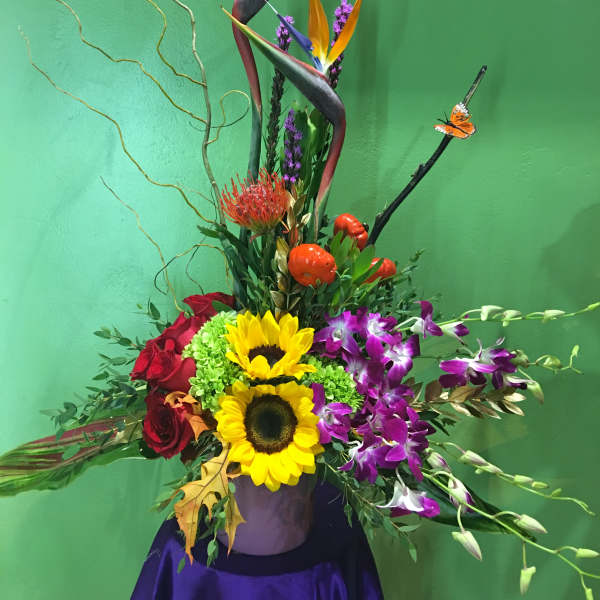 Tropical flower arrangement with sunflowers, orchids, and red roses in a vase