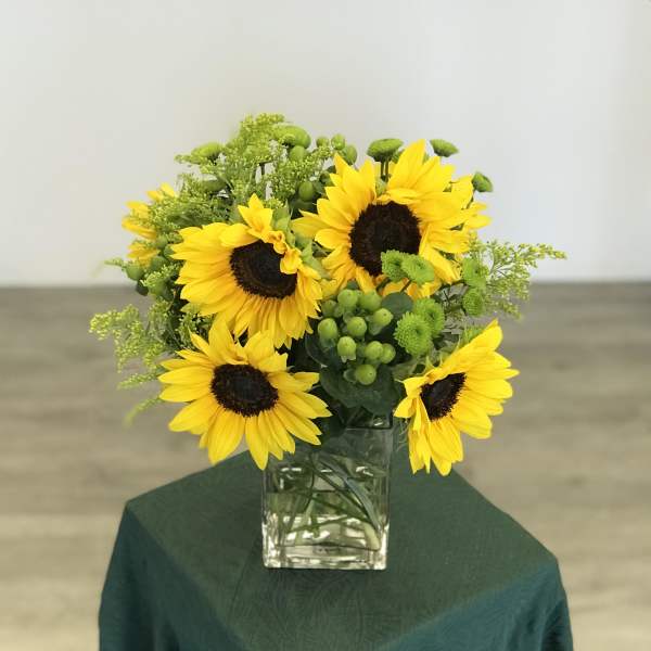 Sunflower arrangement in a clear glass vase with green accents