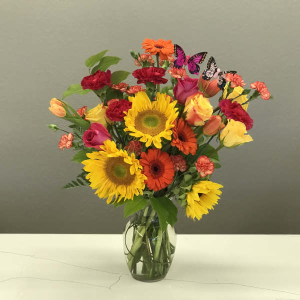 Bright mixed bouquet with sunflowers, roses, gerbera daisies, and carnations in a glass vase