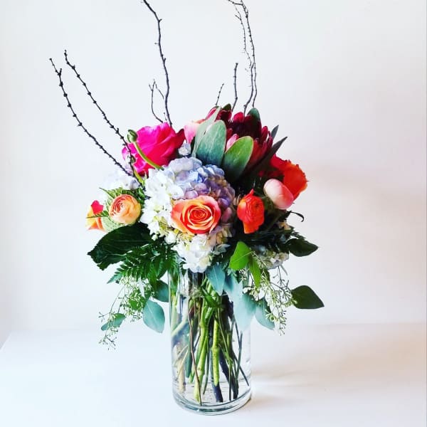 Mixed bouquet of roses, hydrangea, and protea in a clear glass vase