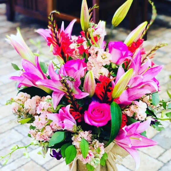 Pink lilies and roses arranged in a burlap-wrapped bouquet