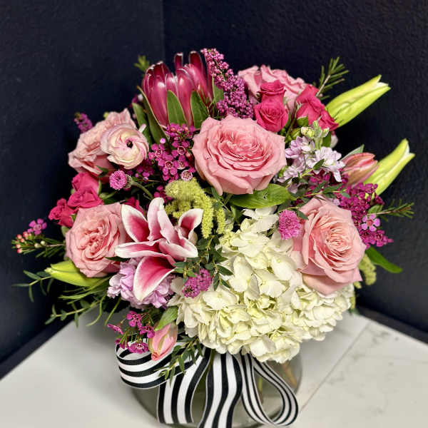 Pink and white floral arrangement in a round vase with a striped ribbon