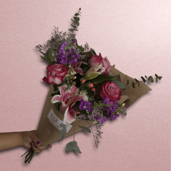 Handheld bouquet of pink roses, lilies, and purple flowers in brown paper