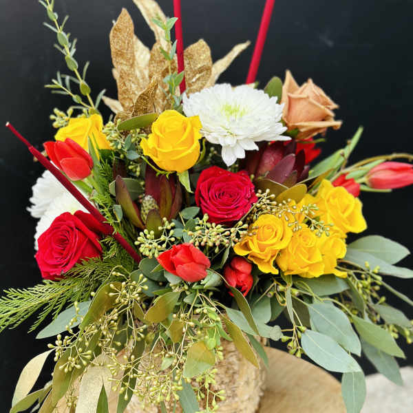 Mixed bouquet of red, yellow, and white flowers in a rustic container