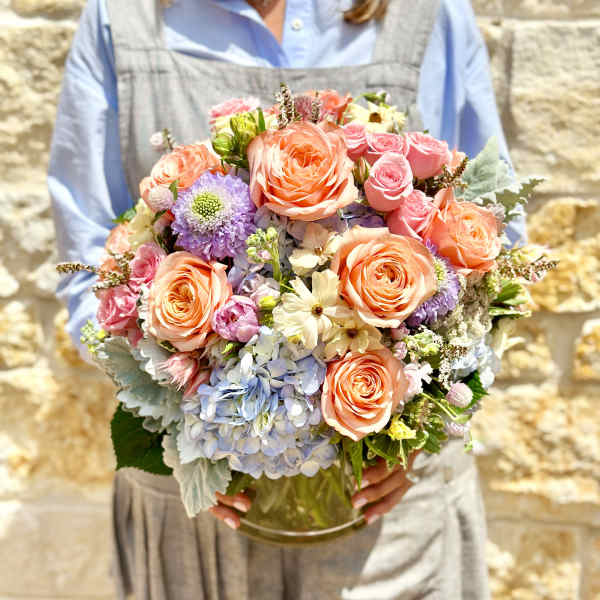 Handheld bouquet of peach and pink roses with pastel blooms