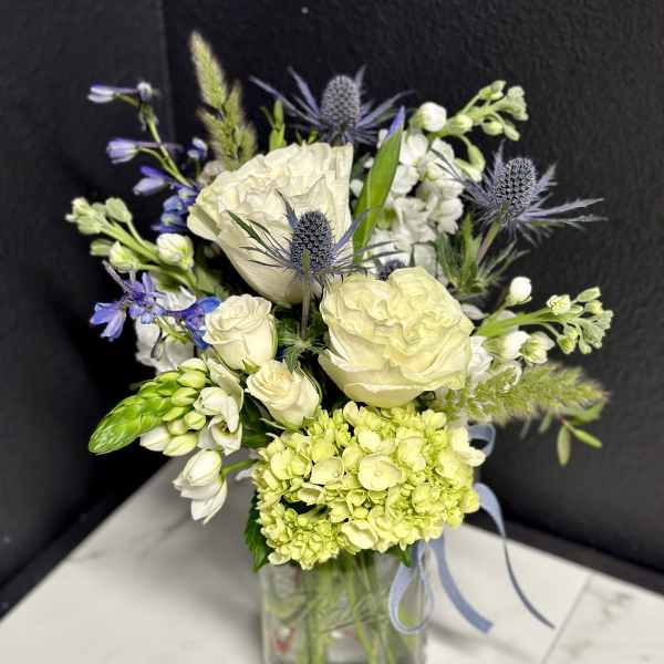 White and pale green bouquet with blue accents in a glass vase