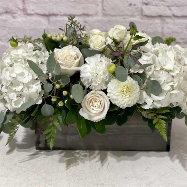 White floral arrangement in a rectangular wooden box with roses and hydrangeas