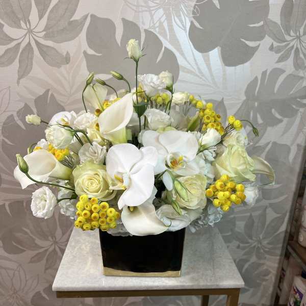 White floral arrangement with calla lilies, roses, and yellow accents in a black vase