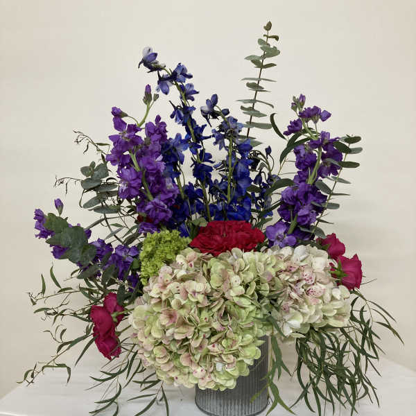 Mixed bouquet with hydrangeas, roses, and tall purple blooms in a metal vase
