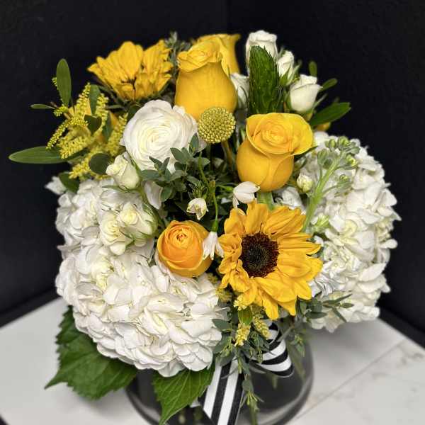 Yellow roses and sunflowers arranged with white hydrangeas in a black vase