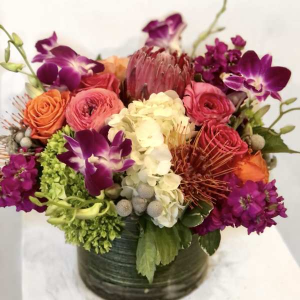 Mixed bouquet in a dark round vase with purple orchids and pink, orange, and white blooms