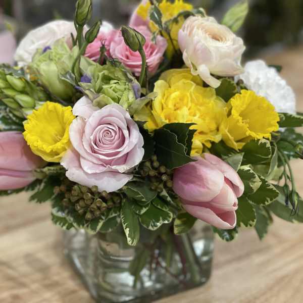 Mixed bouquet of pink roses, yellow blooms, and tulips in a glass vase
