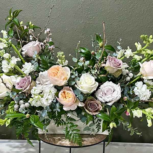 Large pastel floral arrangement with roses and white blooms in a low container